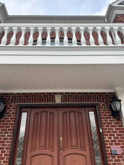 Close-up view of a brick home's entry with a wood double door and a white balustrade balcony above.