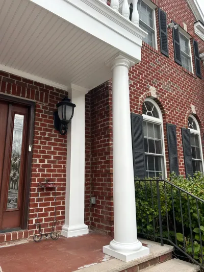 Brick colonial home entrance with white columns, a covered porch, and arched shuttered windows.
