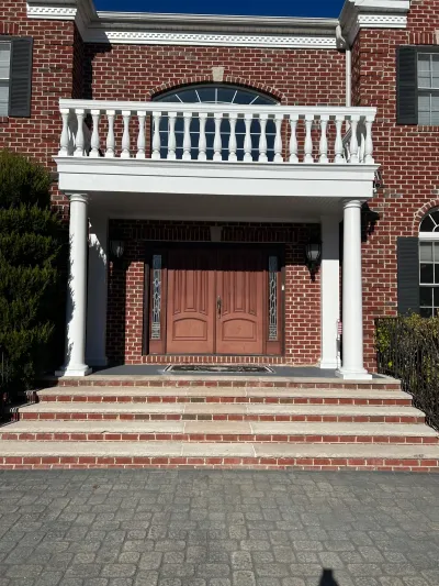 Brick home entrance with white columns, balcony balustrade, and a wood double door.
