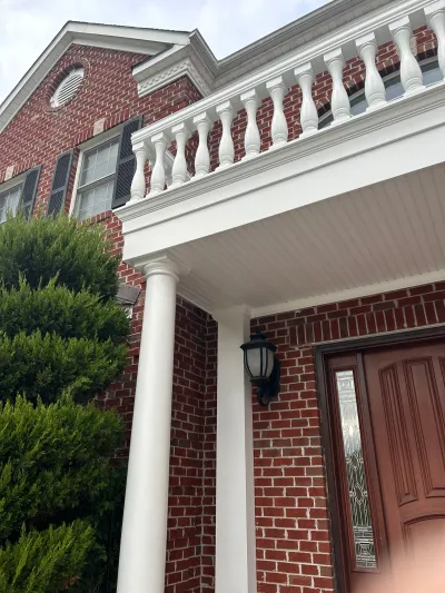 Close-up of a brick home's front porch with white columns and a balcony with turned balusters above.