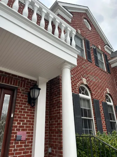 Close-up view of a brick home's white columned entry porch with balustrade railing and arched windows above.