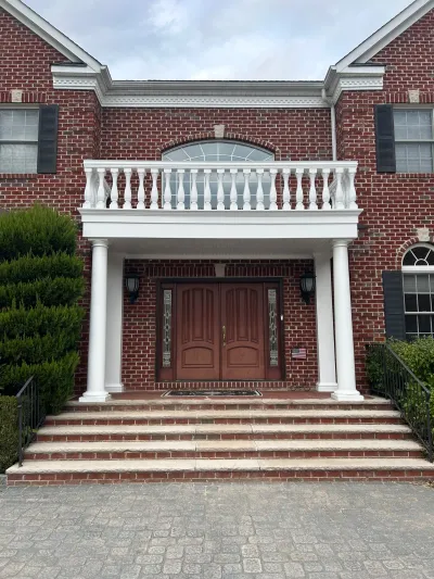 Brick colonial home entrance with white columned portico, balcony, and double wood front doors.