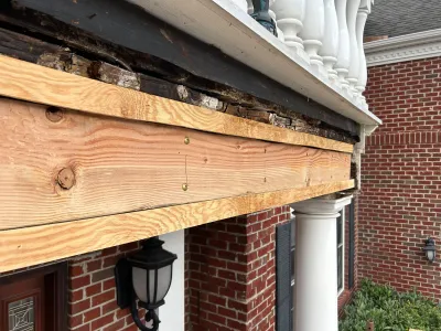 Close-up of rotted porch fascia wood being replaced with new lumber on a brick home.