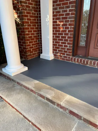 Front porch with white columns, brick walls, and a newly painted grey concrete floor.