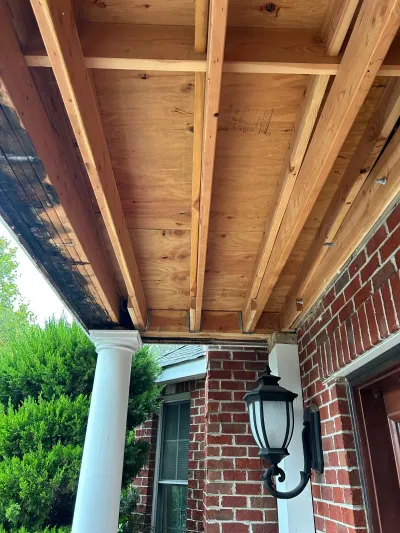 New wood framing replaces old weathered boards on a brick house porch ceiling.