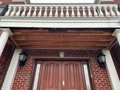 Brick home entryway with exposed rafters above the door during soffit repair, flanked by white columns.