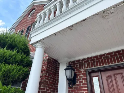 Close-up of a home's front porch roof showing peeling paint and water damage above the entry door.