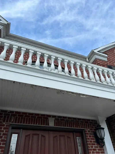 Looking up at a brick home's second-story balustrade and porch ceiling with peeling paint.