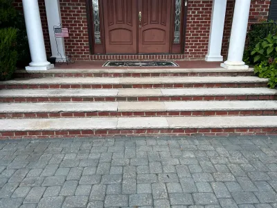 Brick front steps with stone treads lead up to a double wood door flanked by white columns.