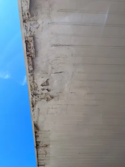 Close-up of a deteriorated stucco corner with cracking and water staining beneath a roof overhang.