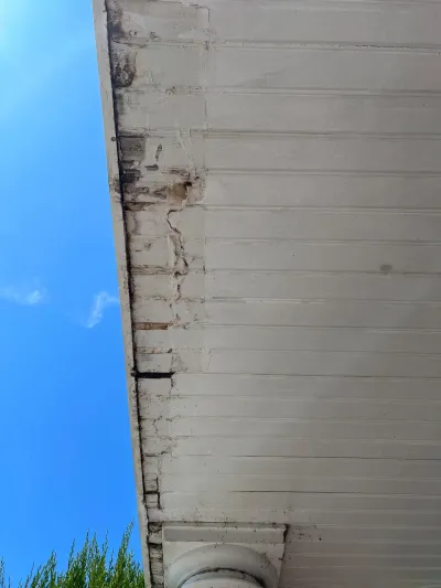 Close-up of a porch soffit and fascia board showing water staining and cracked, rotting wood.