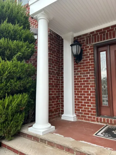 Covered brick entry porch with white round columns, a black lantern sconce, and a glass-panel front door.
