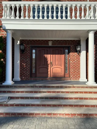 A brick home's covered entry with a mahogany double door, white columns, and a balcony above.