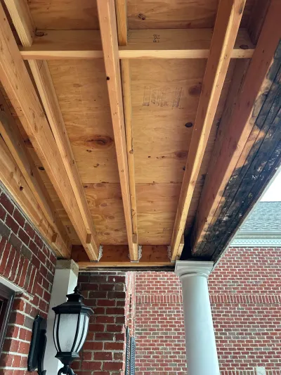New wood porch framing installed next to old rotted framing beside a brick house wall.