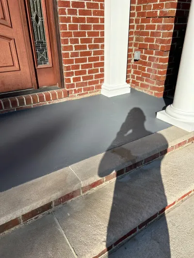 Front porch with charcoal-painted concrete floor, brick walls, and a wood entry door with glass sidelight.