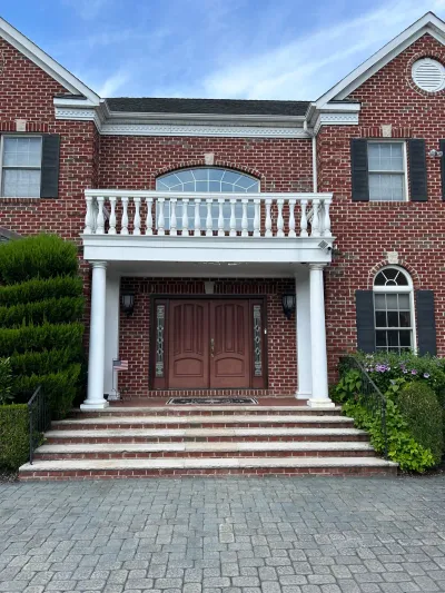 Brick colonial home entrance with a columned portico, balcony, and dark wood double front door.