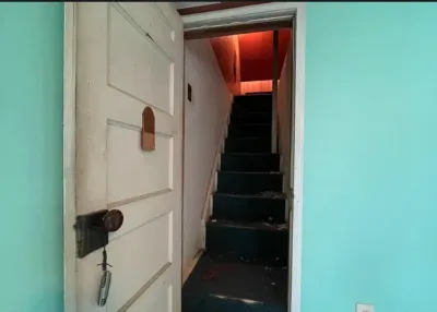 An open door reveals a steep, debris-covered staircase painted black inside a home before renovation.