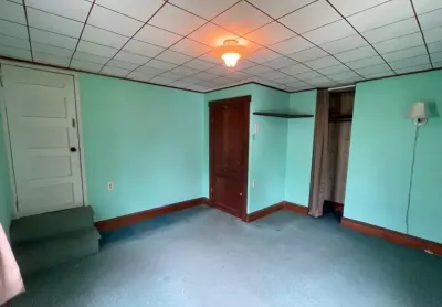 Basement room with green walls, drop ceiling, teal carpet, and a curtained closet opening before renovation.