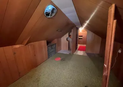 Dated wood-paneled attic space with a sloped ceiling, worn carpet, and a cracked round window.