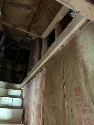 Basement framing during renovation with pink R13 fiberglass insulation partially installed between studs and joists.