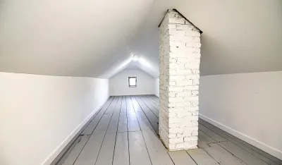 An attic space with sloped ceilings, a painted brick chimney, and a small window letting in light.