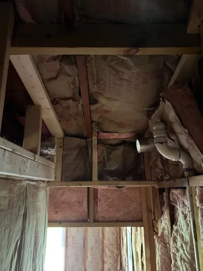 Exposed ceiling and wall framing with fiberglass insulation and a plumbing vent pipe during a remodel.