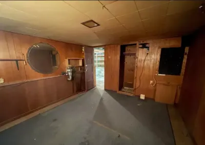Dated wood-paneled basement room with worn carpet and an open exterior door letting in daylight.