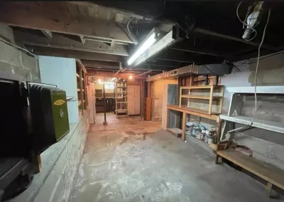 Unfinished basement with concrete floor, exposed joists, stone walls, and wooden storage shelving.