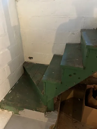 Worn green-painted wooden basement stairs against exposed painted concrete block walls before renovation.