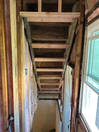 A gutted stairwell under renovation with exposed wood framing, insulation, and stair stringers.