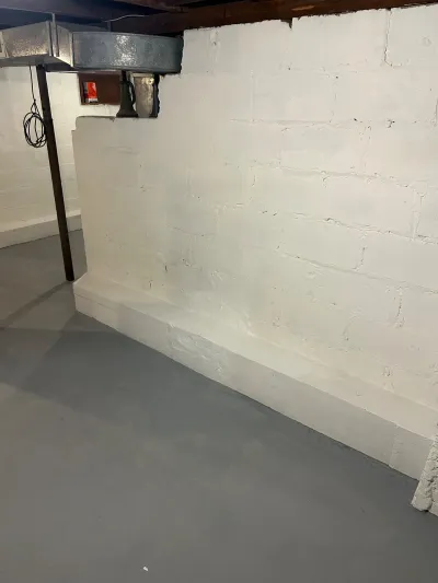 Unfinished basement with painted concrete block walls, painted grey floor, exposed ductwork, and a support column.