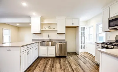 Bright white kitchen with stainless appliances, farmhouse sink, and wood-look flooring.