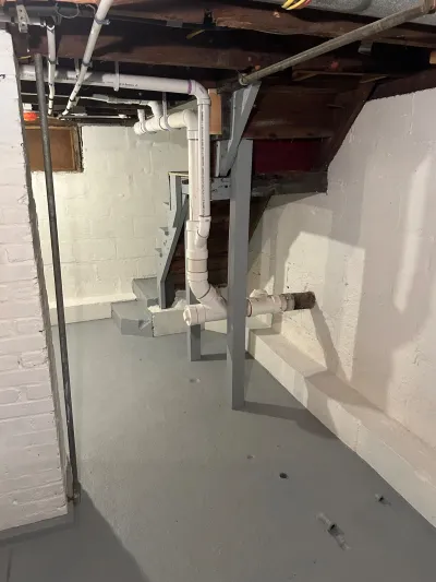 Basement crawlspace mid-renovation with new PVC plumbing, painted walls, and steel support posts.