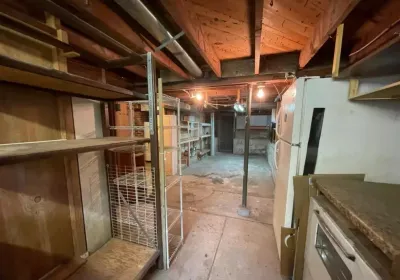 Unfinished basement with exposed joists, concrete floor, storage shelving, and an old refrigerator.