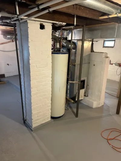 Basement utility area under renovation with water heater, furnace, and exposed ductwork and piping.
