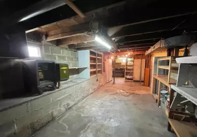 An unfinished basement with exposed joists, concrete block walls, and wood storage shelving.