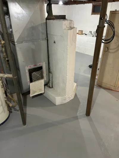 Unfinished basement with a parged masonry pier, furnace, and steel support posts.