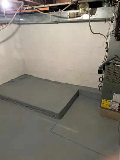 A basement with a freshly poured concrete floor, painted block walls, and a furnace with exposed overhead ductwork.