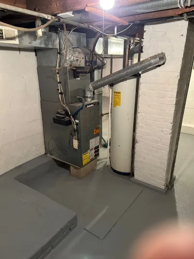 Basement mechanical area with an aging furnace, water heater, and exposed ductwork before renovation.