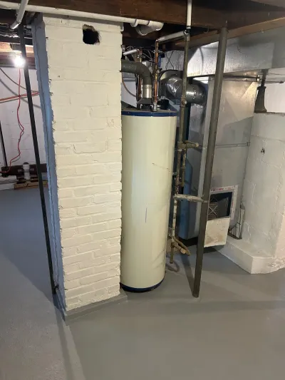 Unfinished basement utility area with an old water heater, furnace, ductwork, and exposed brick chimney chase.