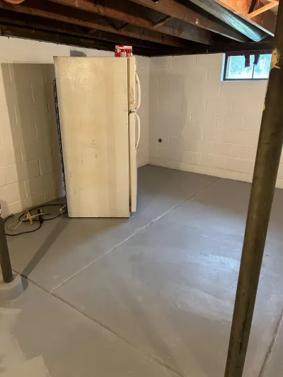 Unfinished basement with painted concrete floor, block walls, exposed joists, and an old refrigerator.