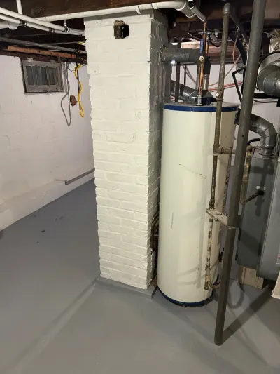 Basement utility area with a water heater, painted brick chimney, and grey coated floor.