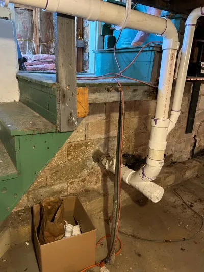 Basement under renovation with newly installed white PVC plumbing pipes along a concrete block wall.