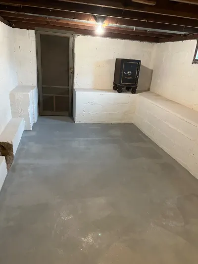Unfinished basement with painted block walls, concrete floor, exposed joists, and an old floor safe on a built-in ledge.