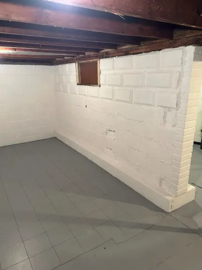 Unfinished basement with painted cinder block walls, exposed floor joists, and gray tile flooring.