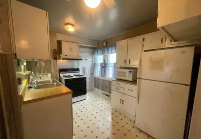 Dated galley kitchen with white cabinets, gas range, and patterned vinyl flooring before renovation.