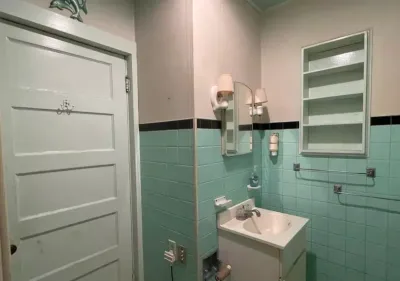 Vintage bathroom with mint green subway tile, black accent band, and an open medicine cabinet before renovation.