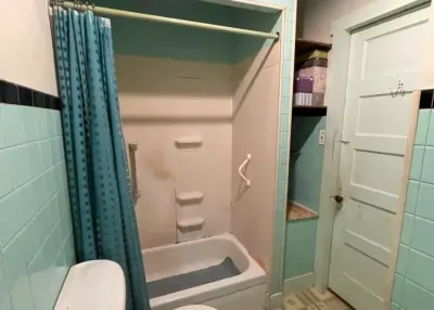 Dated bathroom with mint green tile, black trim, and a fiberglass tub-shower surround with a grab bar.
