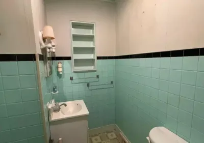 Dated small bathroom with mint green tile, black trim band, and an open medicine cabinet missing its door.