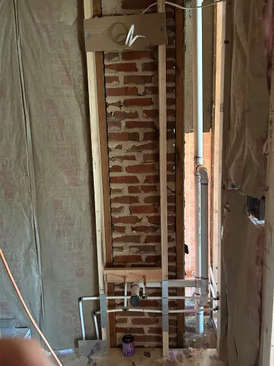Exposed brick wall and rough-in plumbing pipes visible during a mid-renovation wall opening.